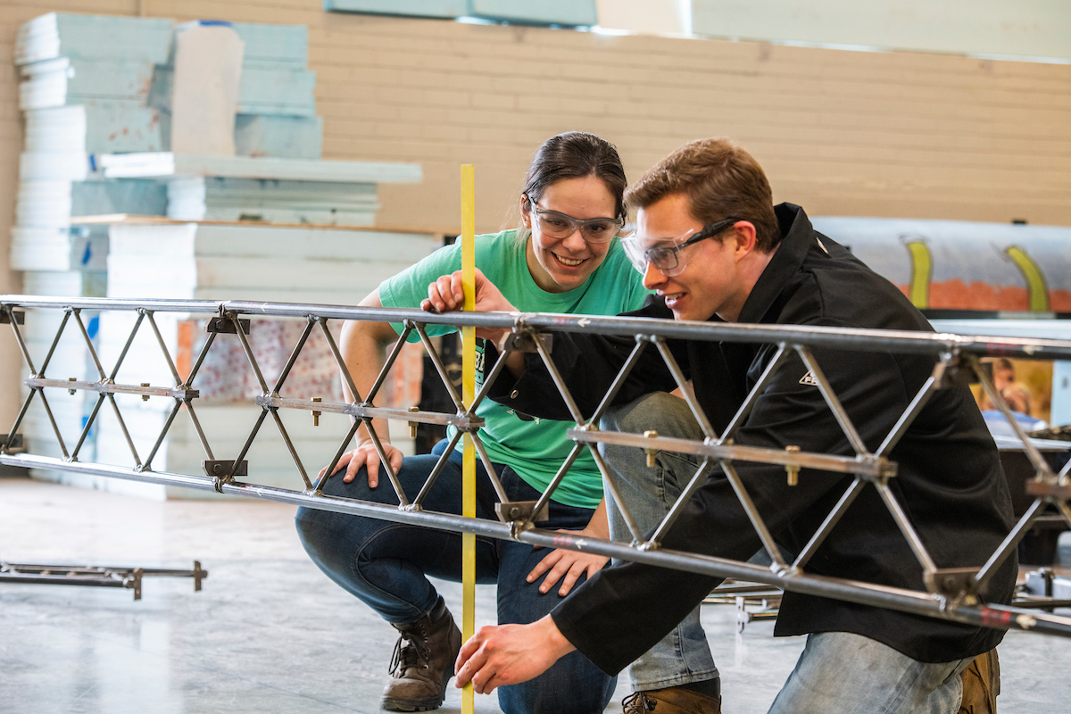 Two students, one male, one female, work together on a steel bridge design